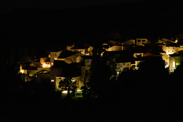 View of traditional houses glowing under warm streetlights in a small village, surrounded by the deep darkness of the night
