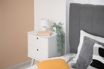 Bedside table with lamp and houseplant near cozy bed in bedroom
