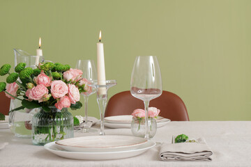 Table served for wedding celebration with candles and flowers near green wall in dining room