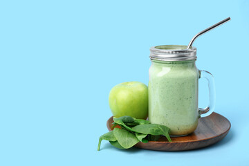 Mason jar of fresh spinach smoothie with apple on blue background