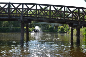 Rustic bridge with wooden railings above peaceful river, water sparkles in sunlight.
