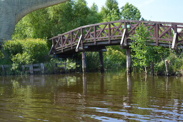 Rustic wooden bridge crossing a calm river surrounded by green trees and reflections.