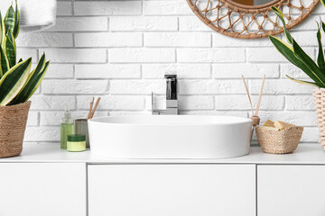 Modern sink, bath supplies and chest of drawers near white brick wall in bathroom