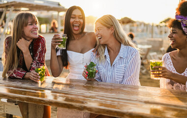 Multiracial happy women friends cheering and drinking mojitos at beach party - Summer lifestyle, travel and vacation concept - Main focus on right blond face girl