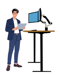 Young businessman in suit and glasses stands with digital tablet near ergonomic standing desk with dual monitors. Modern office, tech-savvy workspace, productivity concept