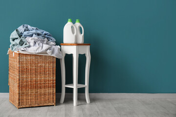 Wicker basket with dirty clothes and bottles of laundry detergent near blue wall