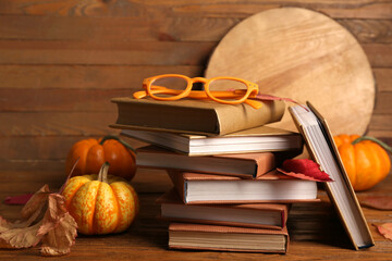 Composition with stack of books, eyeglasses and autumn leaves on wooden background