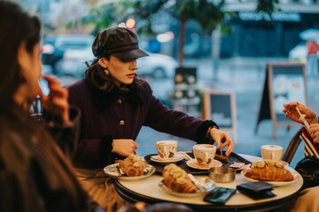 A group of women enjoying coffee and pastries at an outdoor cafe, engaging in casual conversation, surrounded by a bustling urban environment.
