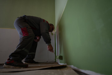 A male worker engaging in interior wall painting, utilizing a roller brush, applying vivid green...