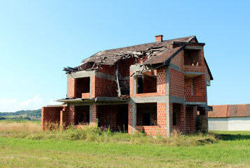 Unfinished two-story brick house with a partially collapsed roof and open windows stands empty in a...