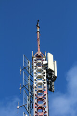 Tall communication tower with red and white lattice structure, multiple antennas, and signal...