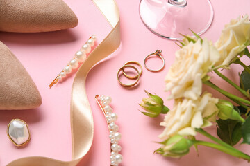Wedding rings with flowers and bride's accessories on pink background, closeup