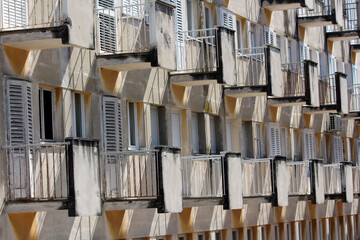 Rows of small balconies with metal railings and faded shutters create a geometric pattern on an old...