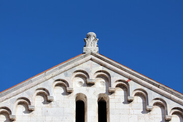 Triangular gable of a Romanesque building features repeating stone arches and a carved finial, set...
