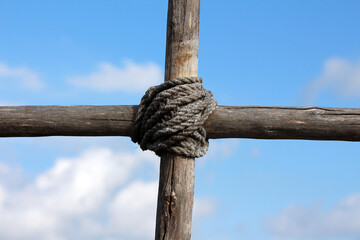 Thick rope tightly binds two weathered wooden beams at a right angle, forming a secure knot against...