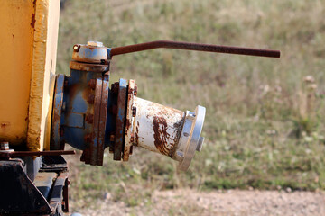 Large industrial valve with blue and white fittings and a long rusty lever is attached to yellow...
