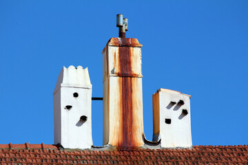 Three white chimneys with rust stains and ventilation pipes stand on a red tiled roof, each with...