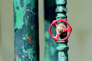 Close-up of a weathered green metal pipe with peeling paint and a red metal valve handle, showing textures and signs of age in bright daylight