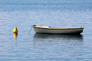 White rowboat floats on calm blue water, tethered to a bright yellow buoy, with gentle ripples...