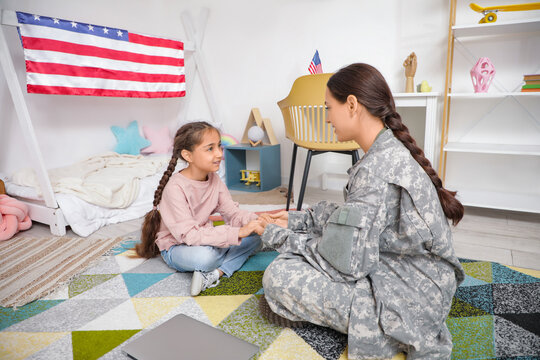 Female soldier with her daughter holding hands in bedroom