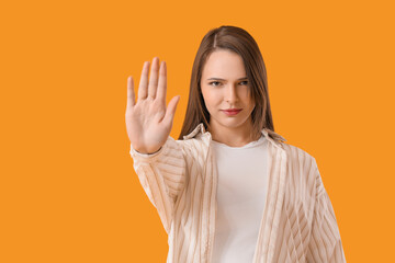 Beautiful young woman showing stop gesture on yellow background