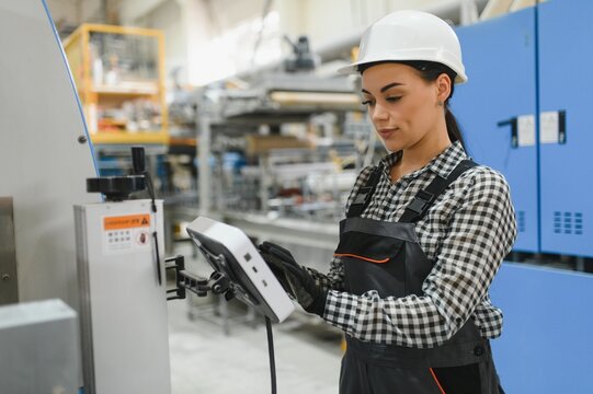 Female factory worker operating machinery using digital tablet in modern industrial plant