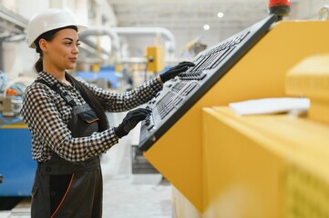 Female factory worker operating machinery control panel in plant