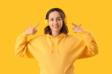 Young woman pointing at headphones on yellow background. Rules concept