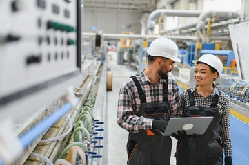 Factory workers using laptop, discussing production line efficiency