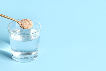 Glass of water and spoon with psyllium husk on light blue background with space for text