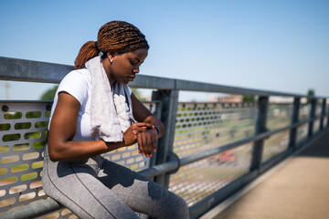 Portrait of exhausted African-American woman in sport clothing looking worried while checking her...