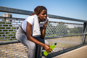 Portrait of tired African-American woman in sports clothing wiping sweat with towel, drinking...