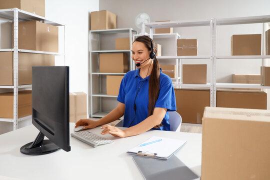 Female worker working with headset and computer at table in warehouse