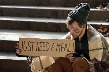 Homeless man holding cardboard with text JUST NEED A MEAL on street