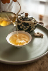 Hands pouring tea from clear glass pitcher into tea cups creating serene tea ritual while soft light and wooden tea tray evoke calming mindful Chinese ceremony atmosphere
