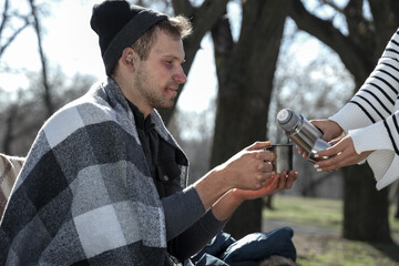 Homeless man with woman pouring hot tea in park