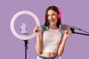 Teenage blogger in headphones recording video on lilac background