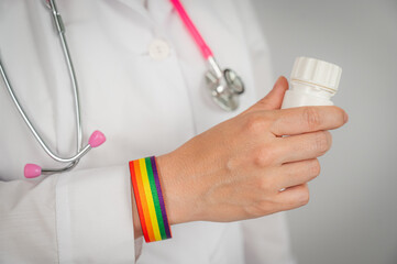 Close up of doctor's hand with rainbow bracelet holding medicine bottle. 