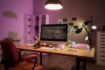 Programmer's desk with computer and glowing lamps in office at night