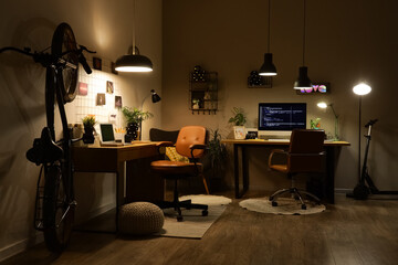 Interior of dark programmer's office with desks, bicycle and glowing lamps at night
