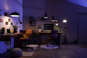 Interior of dark programmer's office with desks and glowing lamps at night