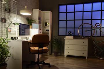 Interior of dark programmer's office with workplace, pin board and glowing lamps at night