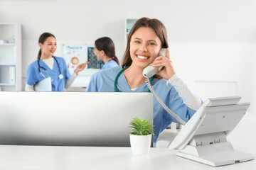 Female medical intern talking by phone at reception in clinic