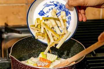 Hand sprinkles vibrant greens and roots into bubbling cauldron, evoking Lunar New Year traditions...