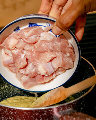 A hand of Middle Eastern descent gently places fresh diced chicken into an aromatic broth, evoking Ramadan and Yalda Night