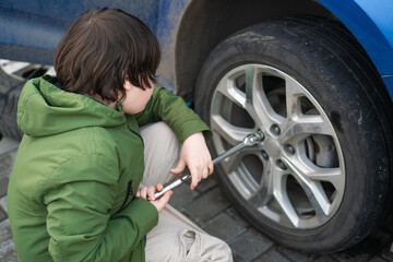 Little boy tightening the screws on the wheel of a blue car