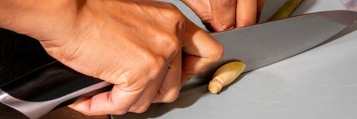 Intricate fingers of a Southeast Asian male slicing lemongrass, evoking Lunar New Year culinary...
