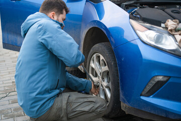 A man tightens the nuts on the wheel of a car