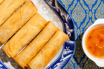 Crispy golden spring rolls nestled on ornate Thai fabric evoke Songkran celebrations and Lunar New...