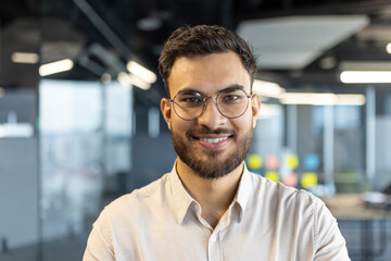 Obraz premium A smiling businessman wearing glasses poses in a modern office setting, showcasing a confident and professional image.